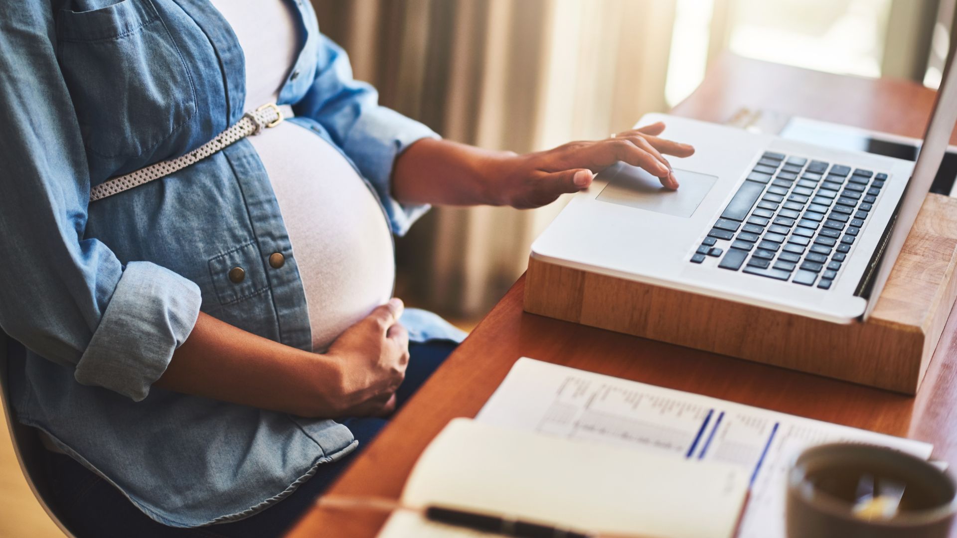 A pregnant woman working at a laptop, she will soon need to go on maternity leave
