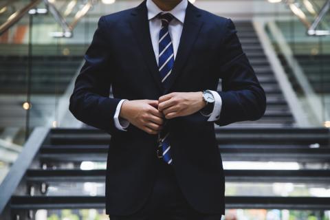 A picture of an attorney in front of steps buttoning his suit jacket