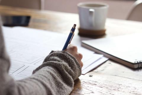 A student studying with coffee, a note pad, a pen and a phone.
